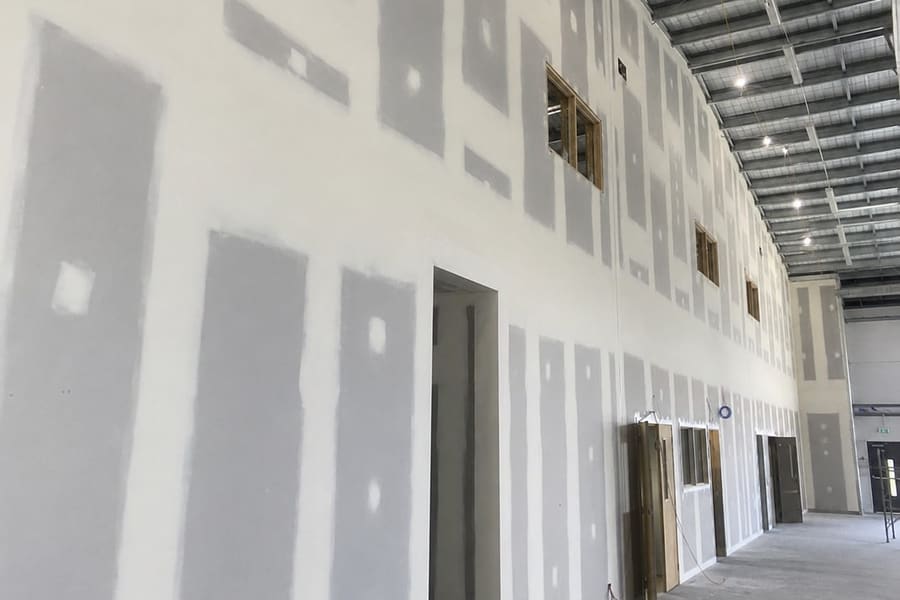 Interior wall of bare plasterboard with visible joints and patched fixings before plastering